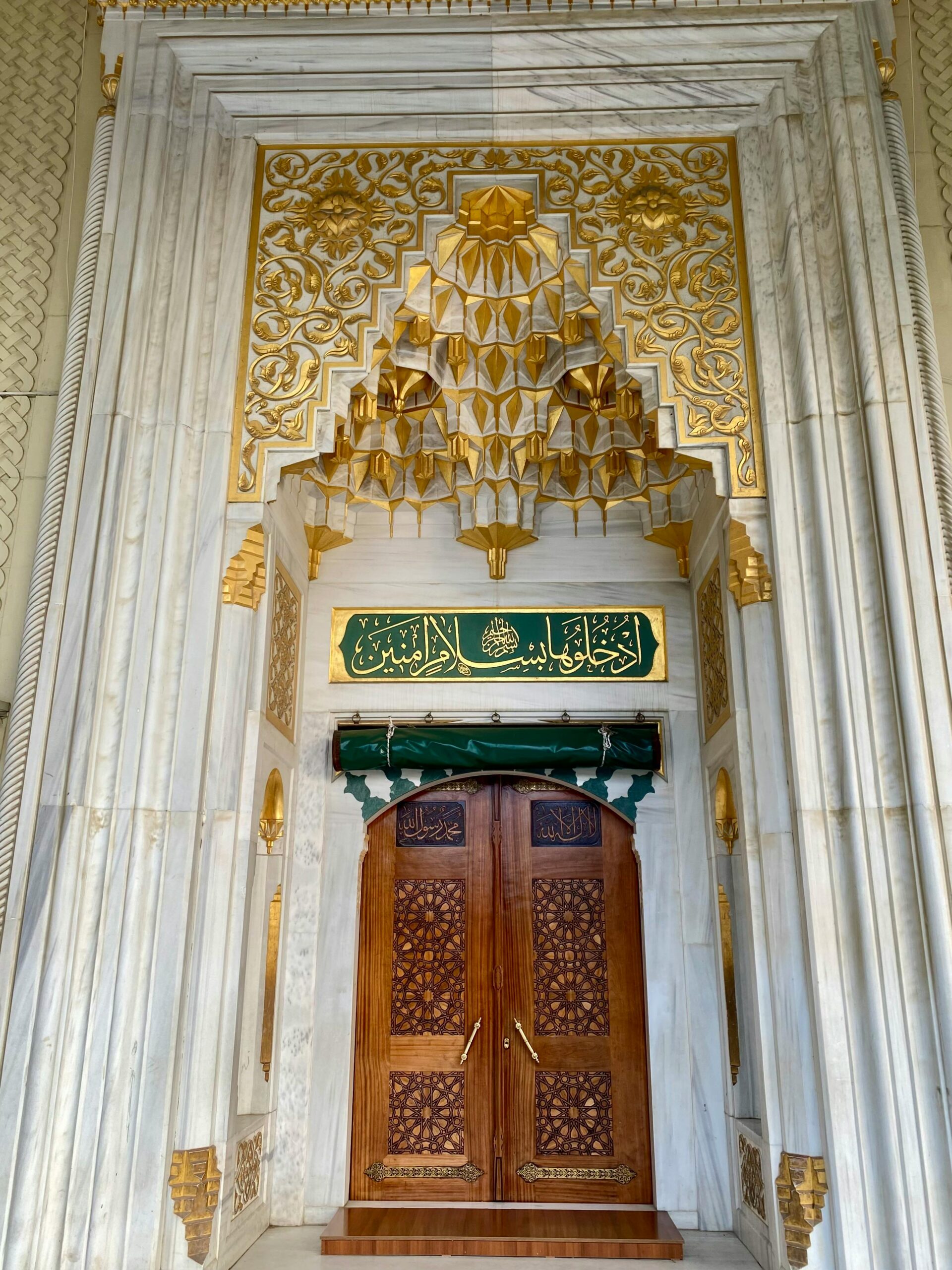 A beautifully designed mosque entrance with gold and marble detailing presents a rich, Islamic architectural style.